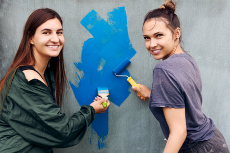 Using blue paint to painting gray wall, smiling young women working as house painters.の写真素材