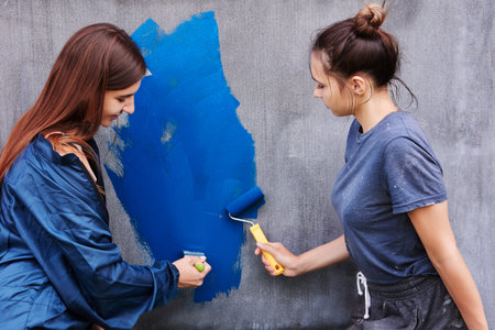 Using paint roller and brush, women painting gray wall with blue paint.の写真素材