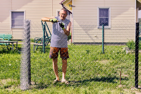 Homeowner unwinds chain link fence roll and twists loose ends of wire together using pliers.