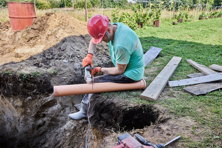 Worker uses an abrasive wheel on an angle grinder to cut off section of plastic sewer pipe.の写真素材