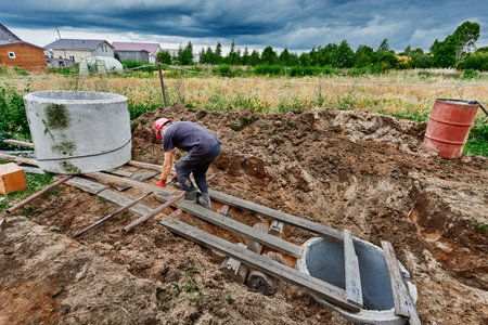 Worker moves concrete ring for septic tank along rollers made of steel pipes.の写真素材