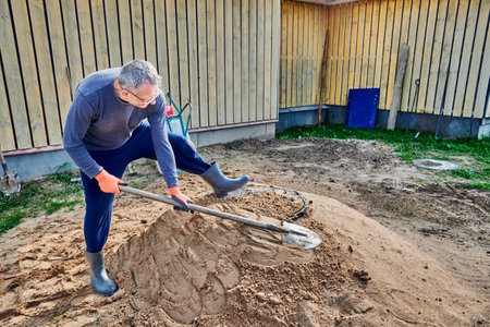 Builder compacts sand near septic tank manhole cover, patting its surface with shovel.の写真素材