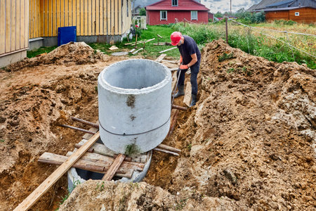 During installation of an autonomous sewage system, worker pushes concrete rings of septic tank onto each other using roller deck.の写真素材