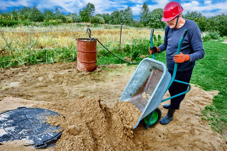 Construction worker pours sand from wheelbarrow around manhole cover.の写真素材