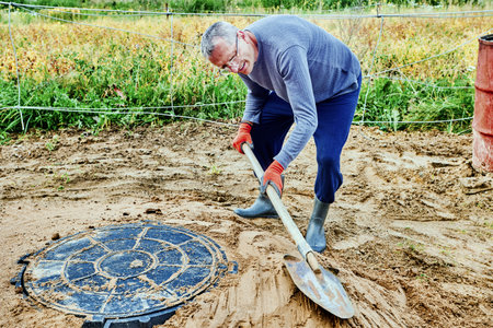 Builder poured sand around manhole cover and ramms it with shovel.の写真素材