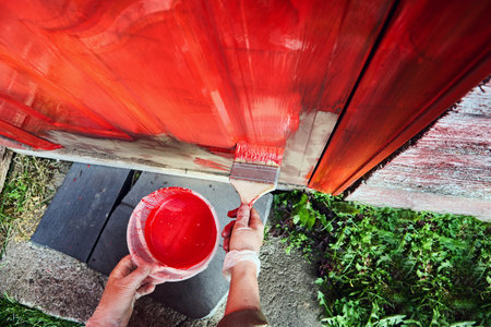 Saturation bright red paint is applied to entrance door of an old farmhouse with wide flat brush.の写真素材