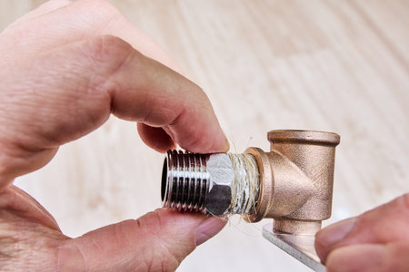 Hex nipple barrel reducer adapter is being sealed with plumbing hemp and screwed into brass elbow fitting, ensuring secure threaded joint in pipe fitting.の写真素材