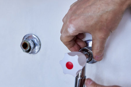 Hands carefully connect new dual handle faucet to exposed plumbing outlet in white wall, aligning fitting and ensuring tight seal with visible metal cover.の写真素材