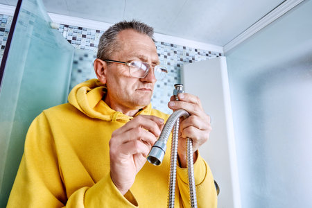 Plumber checks sealing washer on end of shower hose while preparing to install replacement due to...