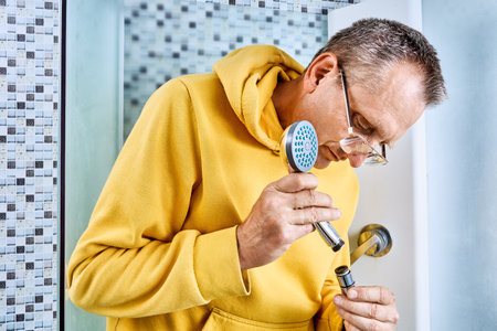 Screwing showerhead onto end of hose, maintenance worker completes final connection of handheld shower unit during shower fixture replacement.の写真素材