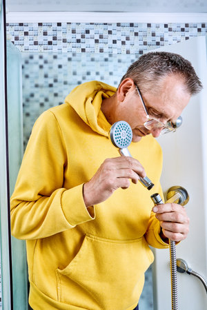 Plumber installs showerhead by screwing it onto hose end with hand while standing inside cabin next to panel, vertical image.の写真素材