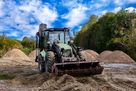 Front end loader carries out sitework with sand piles present on working area.
