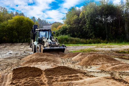 Loader excavator redistributes sand, creating smooth foundation for construction.