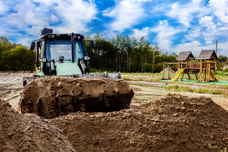 Heavy duty construction loader pushes earth while maneuvering across uneven terrain near wooden play...