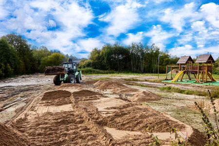 Excavator carries out construction work with sand piles visible on ground surface near playground...