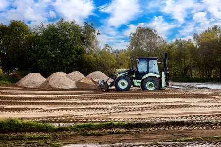Front loader shifts light earth layer forward with bucket edge, focusing on evening out base surface...