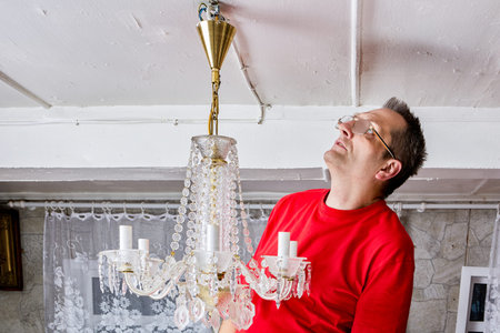Removing crystal chandelier from ceiling, person examining fixture attachment mechanism in domestic...