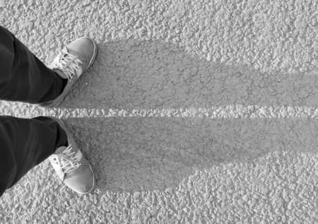 Legs in sneakers cast a shadow on the asphalt top view in black and whiteの写真素材