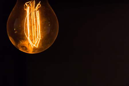 A naked retro light bulb in top left corner of the frame on a black backgroundの写真素材