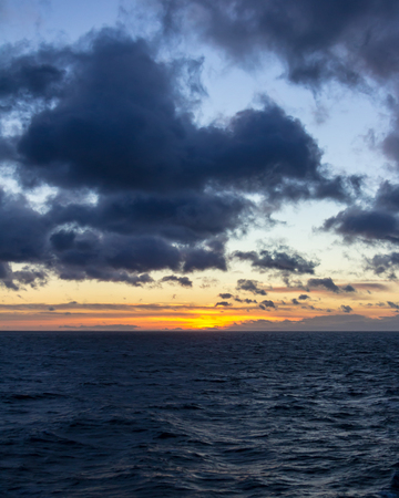 Brilliant orange and yellow sunset at sea with mountains and clouds in silhouetteの写真素材