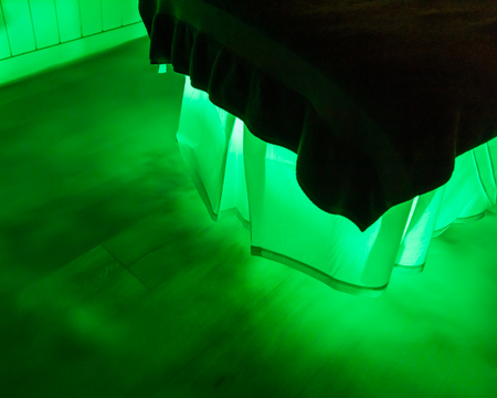 An eerie green glow and mist is coming from under a bed with a white skirt and dark duvetの写真素材