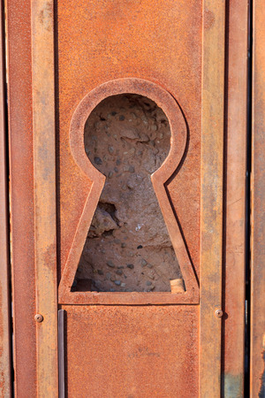 Large keyhole in a rusted metal door with a view of the rock wall behindの写真素材