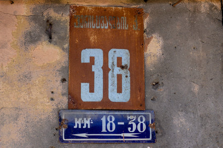 Street number 36 on a metal placard against a stucco wall, white numbers on a red and blue...