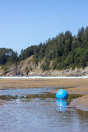 Blue soccer ball sits in one of the pools of the delta of a creek emptying into Smuggler Cove at Short Sand Beach on the Oregon coastの写真素材