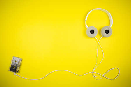 Audio cassette tape and modern headphones on a yellow backgroundの写真素材