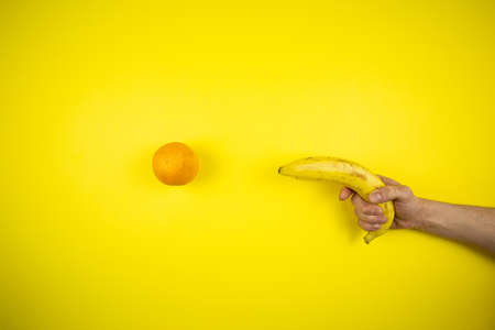Banana shoots an orange on a yellow backgroundの写真素材
