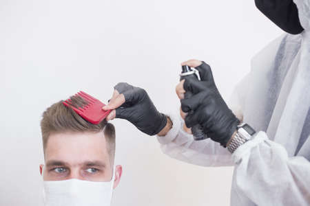 The work of the barber during the coronavirus, the hairdresser trim the client in a mask and a protective suit, quarantineの写真素材