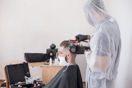 The work of the barber during the coronavirus, the hairdresser trim the client in a mask and a...