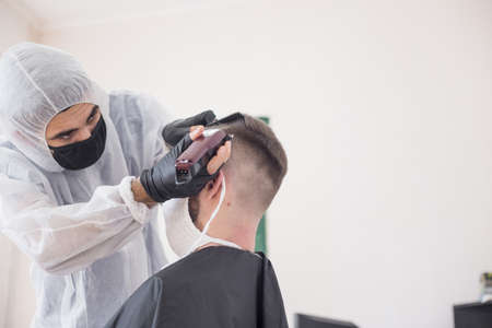 The work of the barber during the coronavirus, the hairdresser trim the client in a mask and a protective suit, quarantineの写真素材