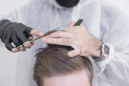The work of the barber during the coronavirus, the hairdresser trim the client in a mask and a...