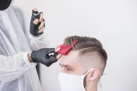 The work of the barber during the coronavirus, the hairdresser trim the client in a mask and a protective suit, quarantineの写真素材