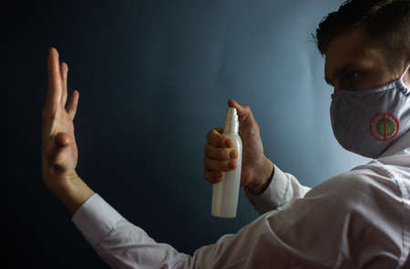 A man in a protective mask against coronavirus sprays an antiseptic on his hands, COVID-19の写真素材