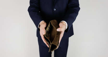 A man in a business suit holds in his hands an empty wallet without money. Financial crisis. Bankruptcy in business. The employer is disappointed.の写真素材