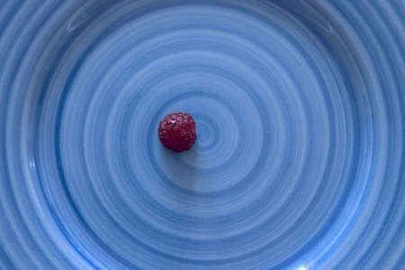 a red raspberry on a blue spiral plateの写真素材