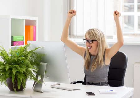 Happy woman sitting at her desk with arms up  の写真素材