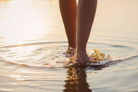 Woman walking on the beach at sunsetの写真素材