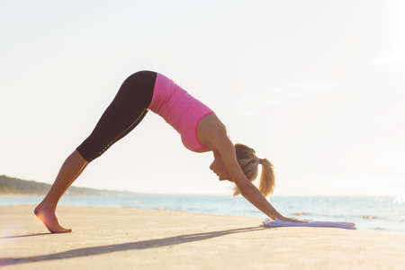 Silhouette of young healthy and fit woman practicing yoga on the beachの写真素材