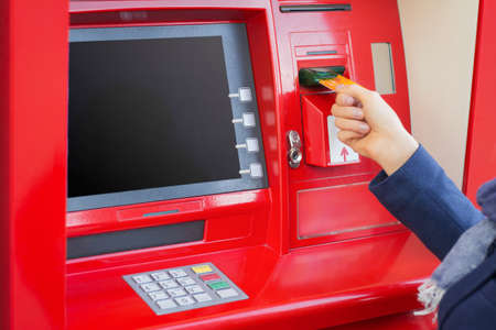 Woman inserting credit card into ATM to withdraw moneyの写真素材