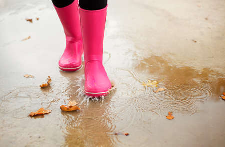 Woman with pink rubber boots walking through puddle in autumnの写真素材