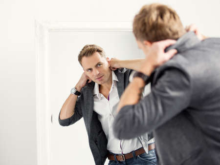 Casually dressed young handsome man in front of mirrorの写真素材