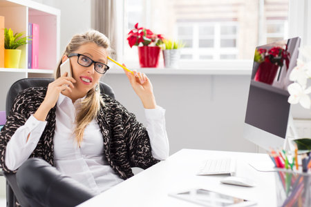 Creative woman talking on phone while sitting at desk in officeの写真素材