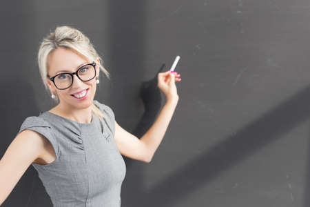 Teacher writing with white chalk on empty blackboard in classroomの写真素材