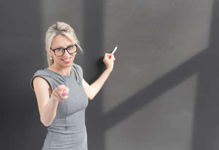 Teacher pointing at camera while writing on blackboard with chalkの写真素材