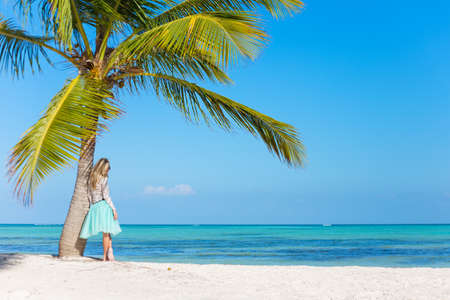 Woman standing under palm tree on tropical beachの写真素材
