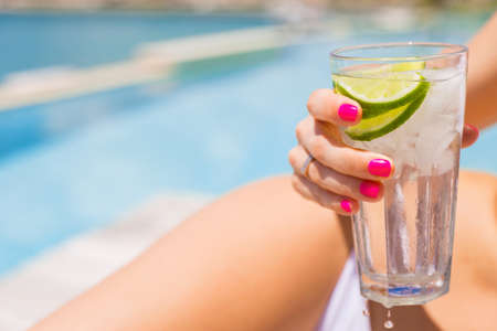 Woman holding refreshing cold drink while sunbathing by the poolの写真素材