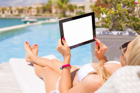 Woman using tablet computer while relaxing by the swimming poolの写真素材